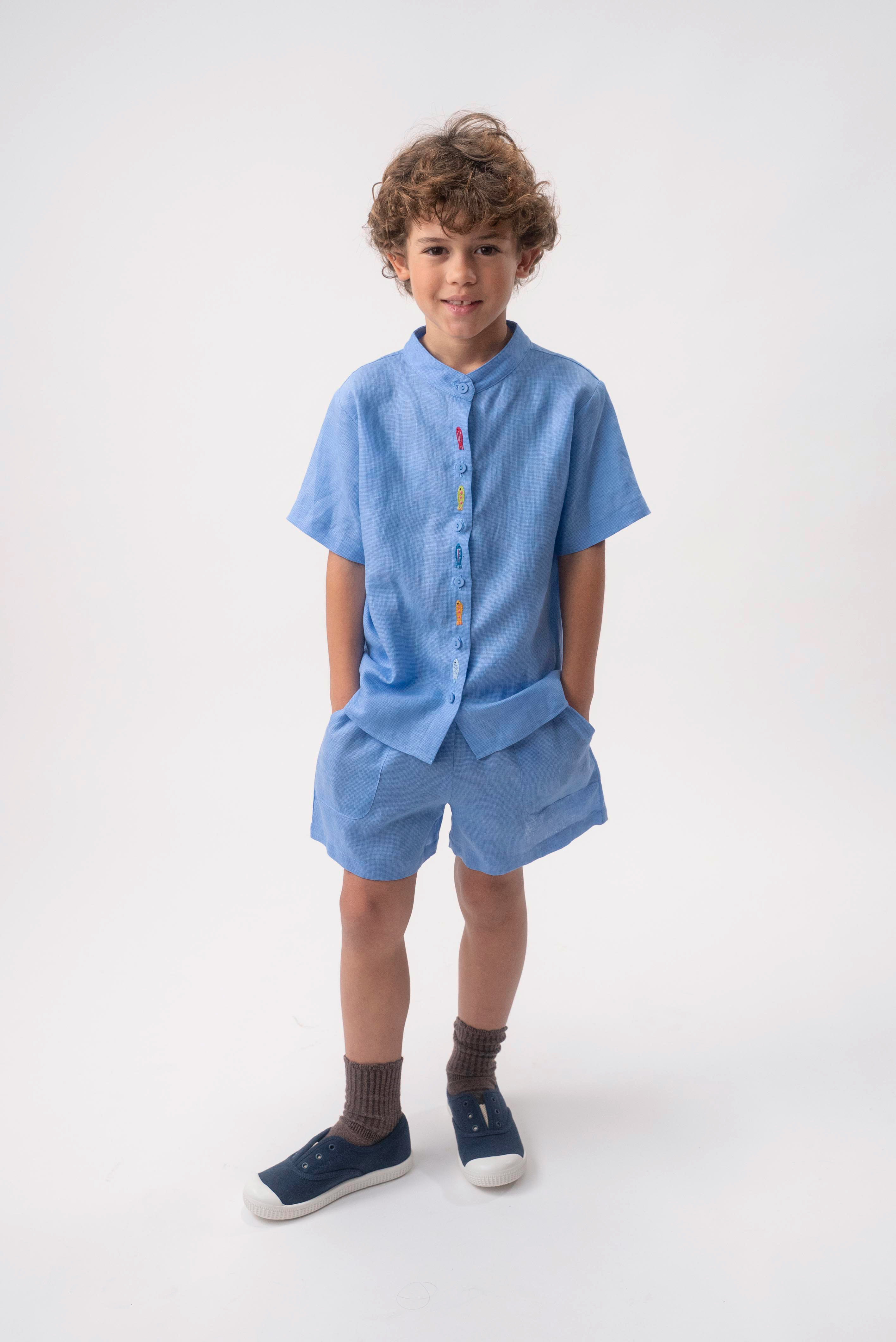 Menino vestindo Shorts Chico infantil em linho azul índigo claro, combinado com camisa azul no mesmo tom.