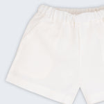 Shorts infantil em linho puro branco com bolsos frontais e cintura elástica para meninos e meninas, visto de frente em detalhe.