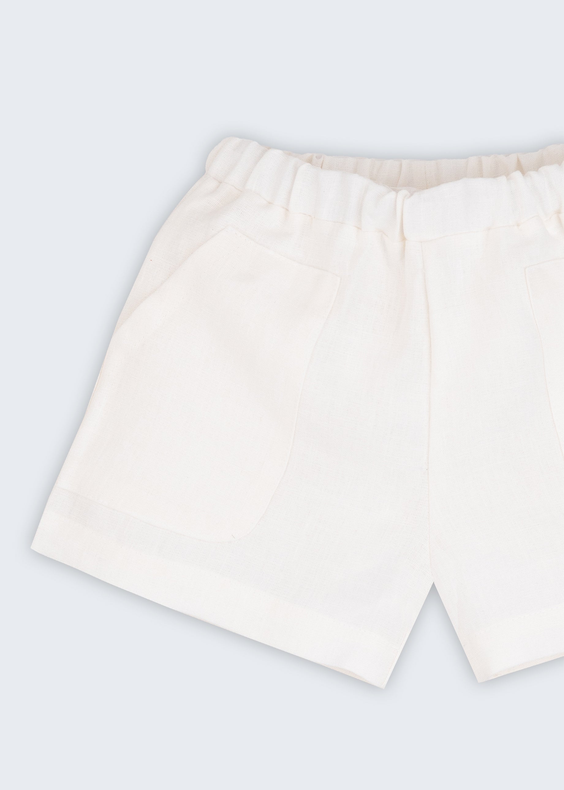 Shorts infantil em linho puro branco com bolsos frontais e cintura elástica para meninos e meninas, visto de frente em detalhe.