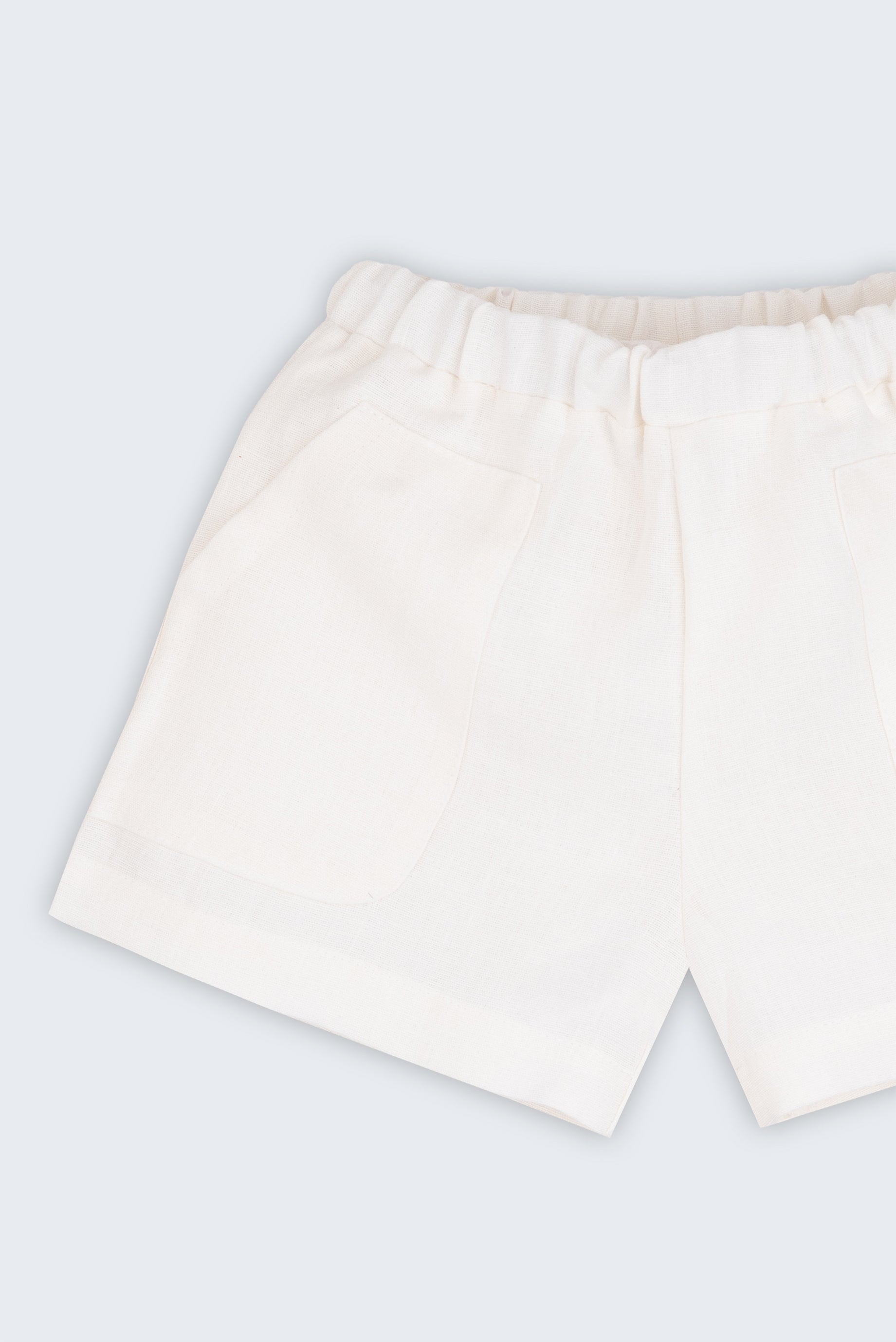 Shorts infantil em linho puro branco com bolsos frontais e cintura elástica para meninos e meninas, visto de frente em detalhe.