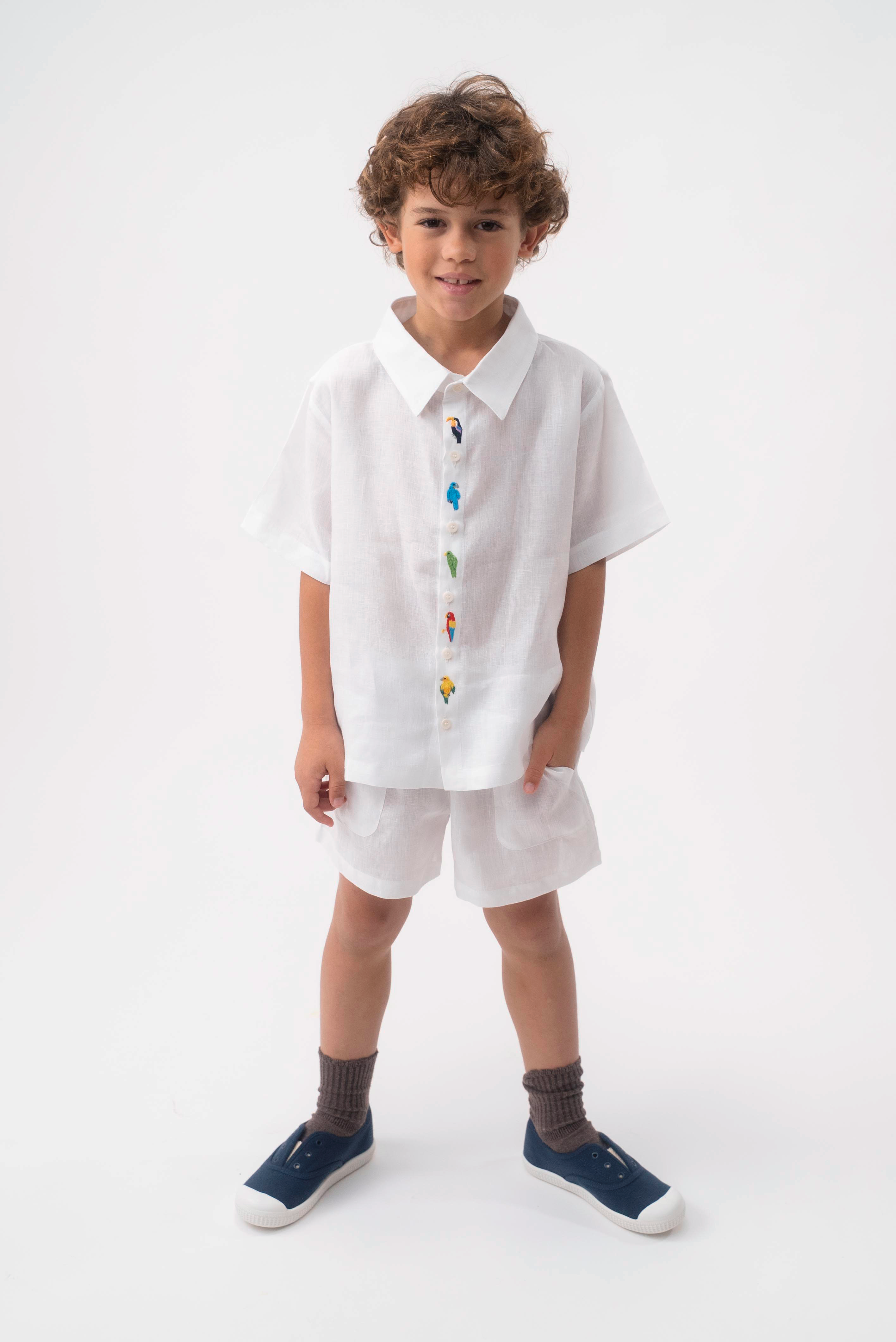 Menino vestindo Shorts Chico infantil em linho branco, combinado com camisa branca bordada, em fundo claro.