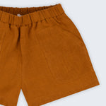 Shorts infantil em linho puro marrom terracota com bolsos frontais e cintura elástica, visto de frente em detalhe.