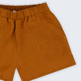 Shorts infantil em linho puro marrom terracota com bolsos frontais e cintura elástica, visto de frente em detalhe.