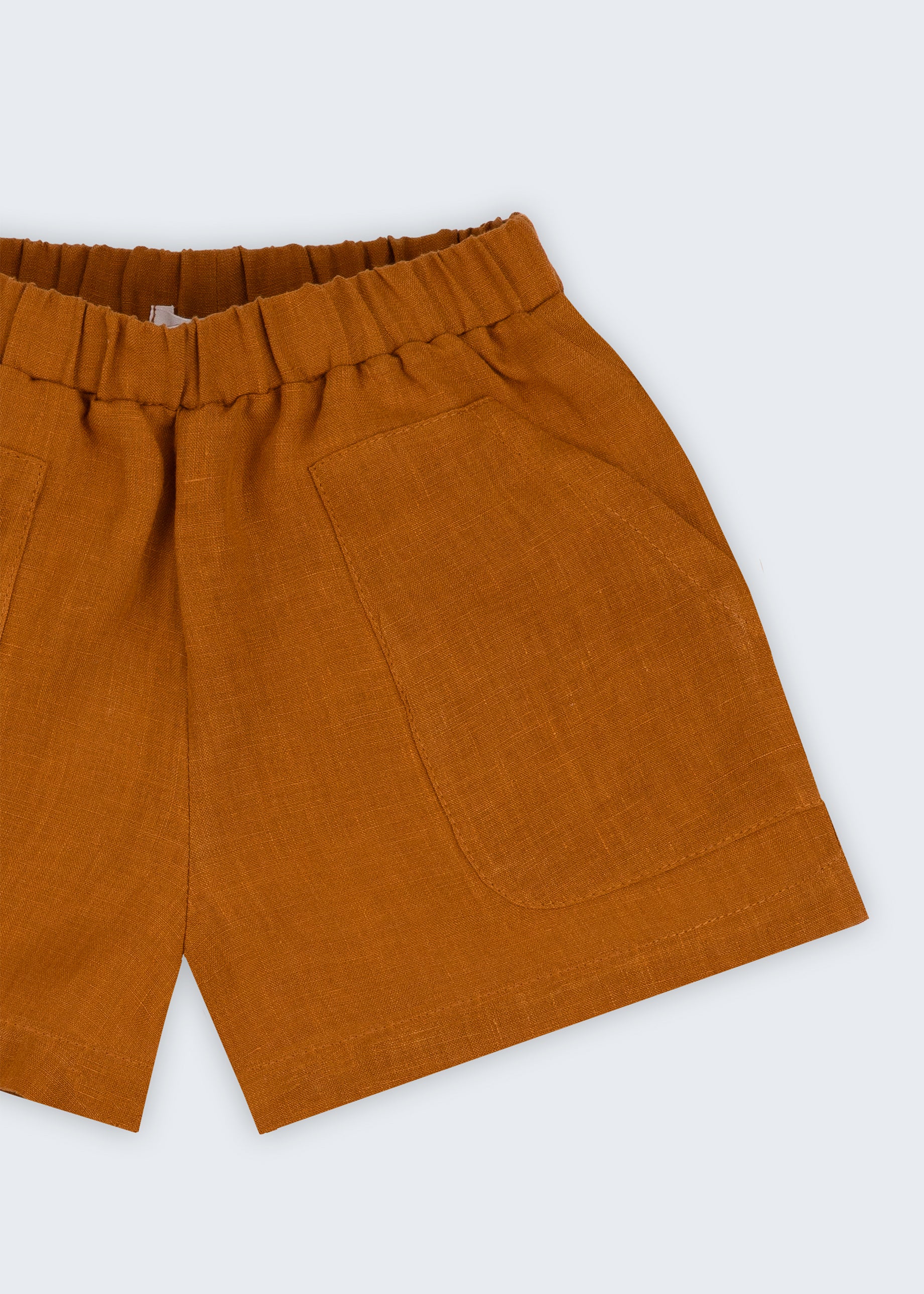 Shorts infantil em linho puro marrom terracota com bolsos frontais e cintura elástica, visto de frente em detalhe.
