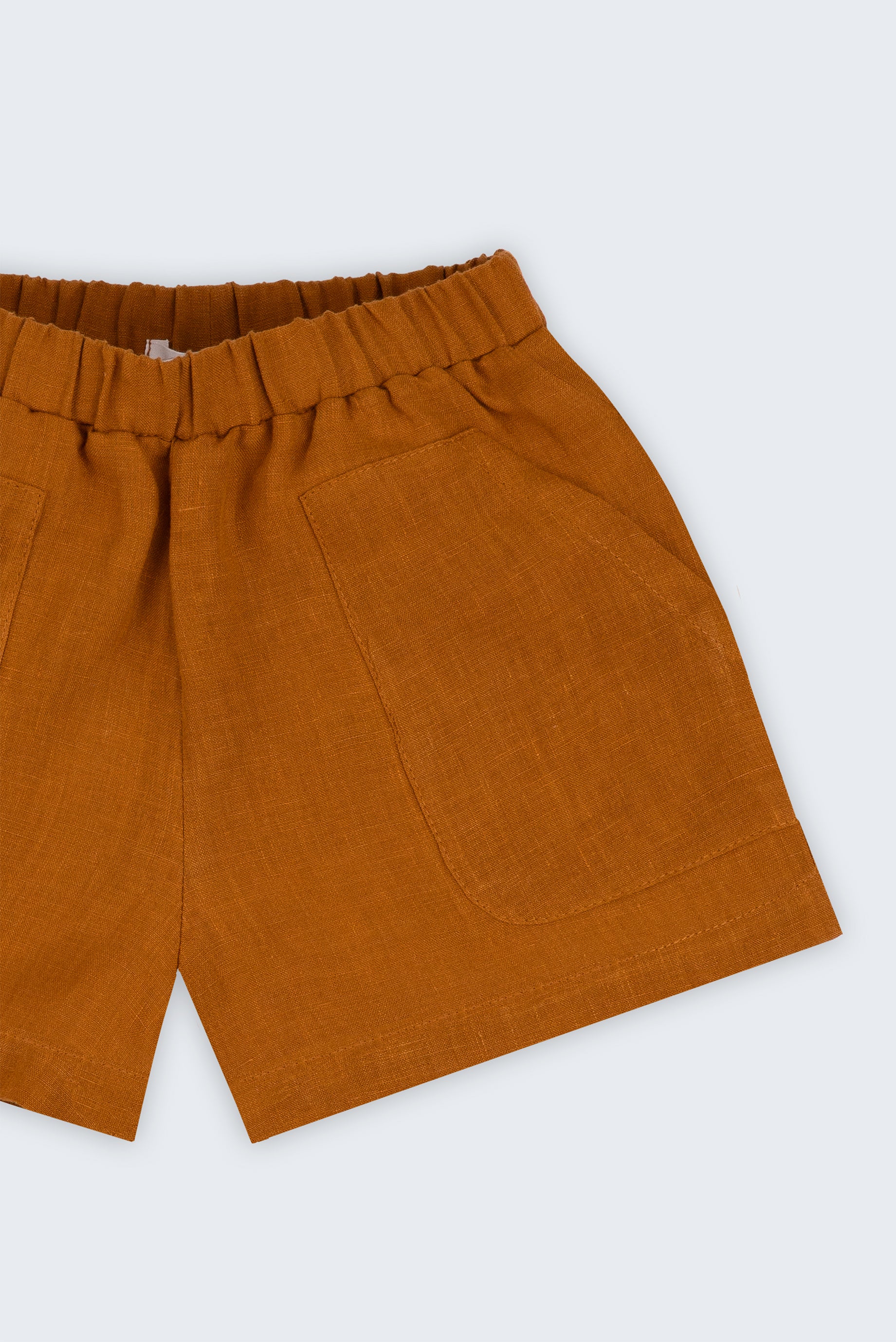 Shorts infantil em linho puro marrom terracota com bolsos frontais e cintura elástica, visto de frente em detalhe.