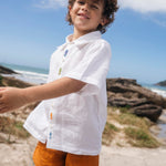 Menino usando shorts infantil em linho puro verde alfazema com bolsos frontais e cintura elástica, fazendo conjunto com camisa branca.