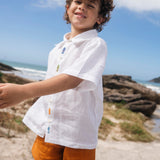 Menino usando shorts infantil em linho puro verde alfazema com bolsos frontais e cintura elástica, fazendo conjunto com camisa branca.