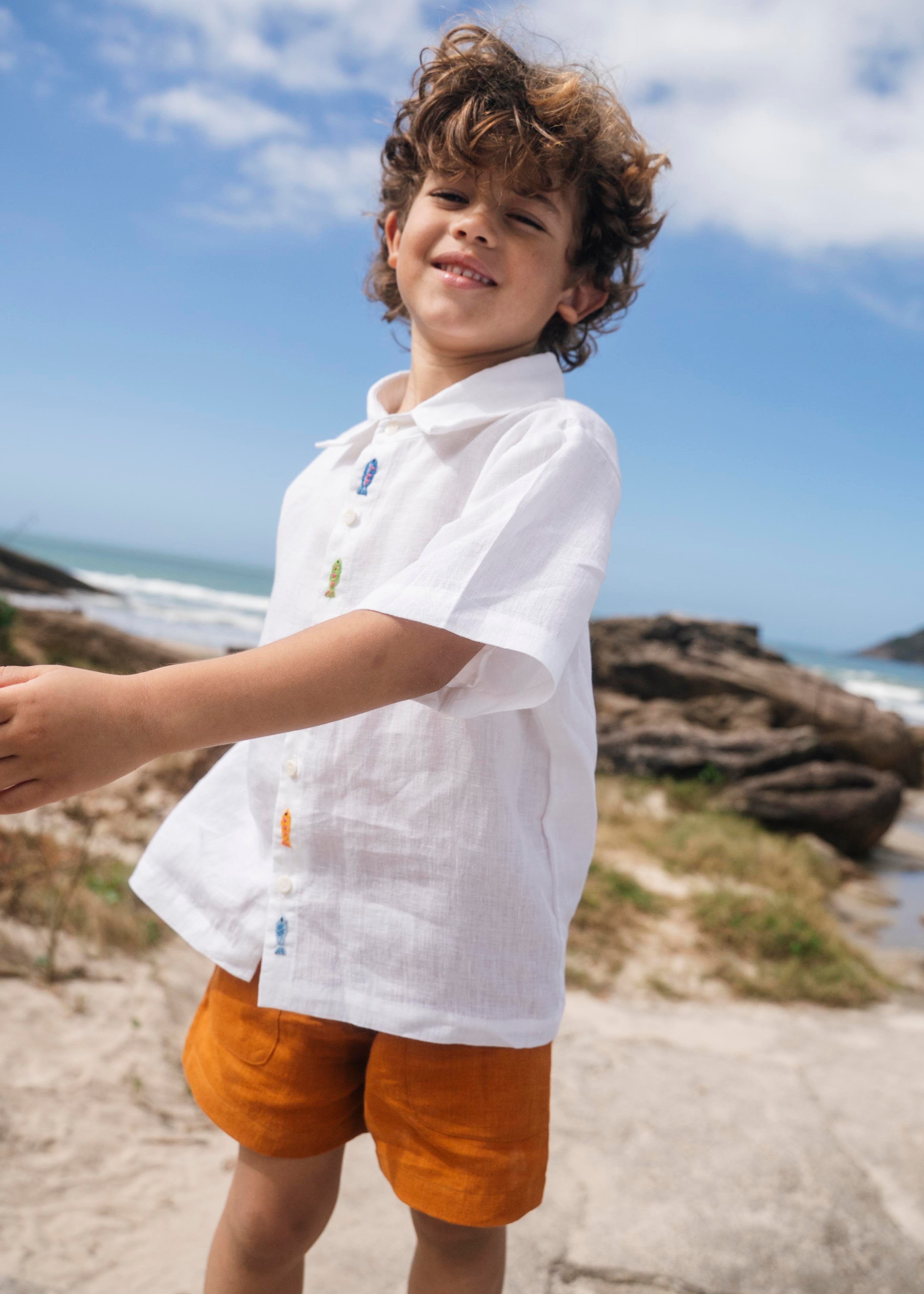 Menino usando shorts infantil em linho puro verde alfazema com bolsos frontais e cintura elástica, fazendo conjunto com camisa branca.