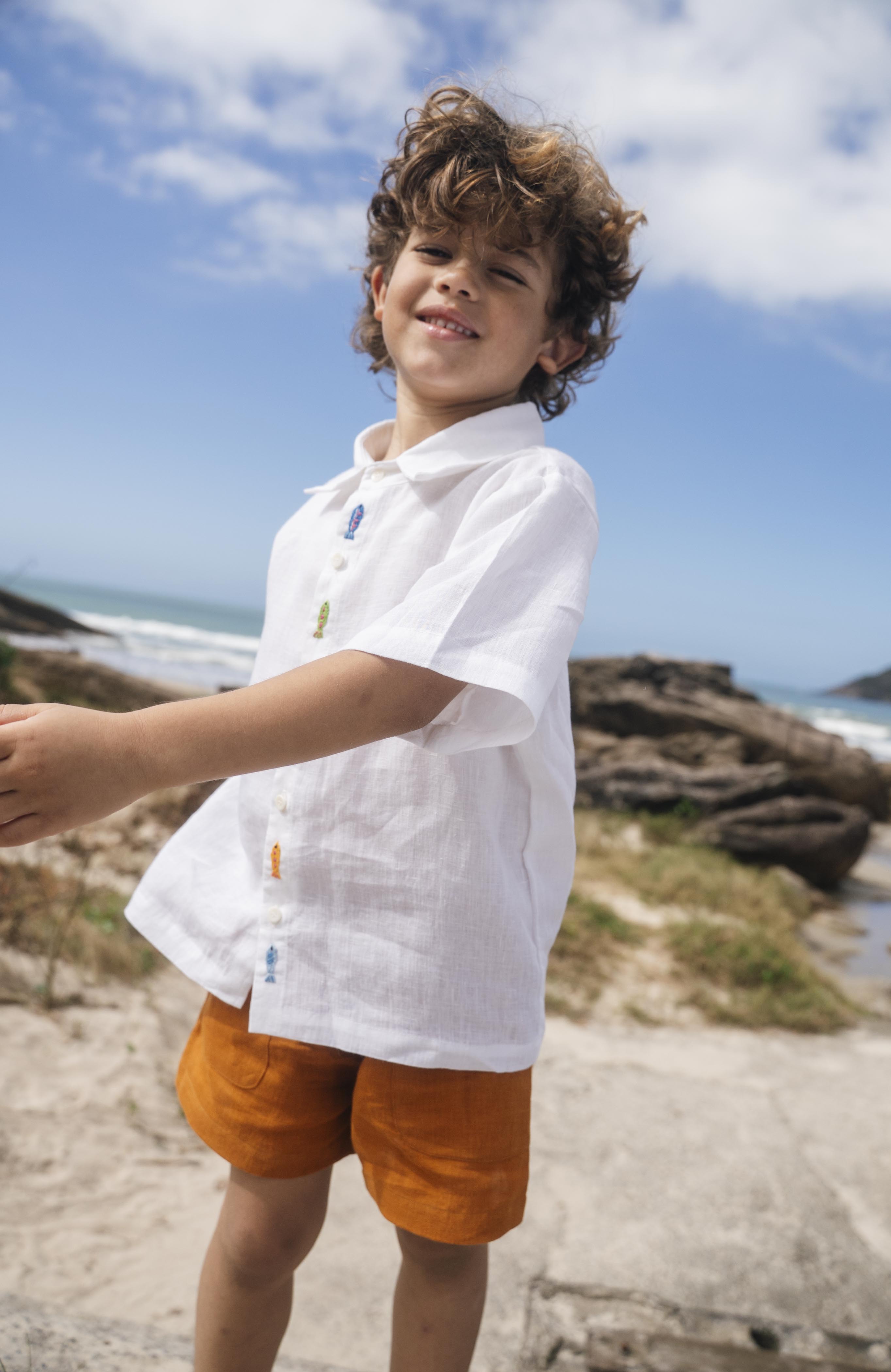 Menino usando shorts infantil em linho puro verde alfazema com bolsos frontais e cintura elástica, fazendo conjunto com camisa branca.