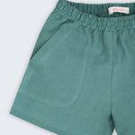 Detalhe do shorts infantil em linho verde com bolso frontal e textura natural do tecido