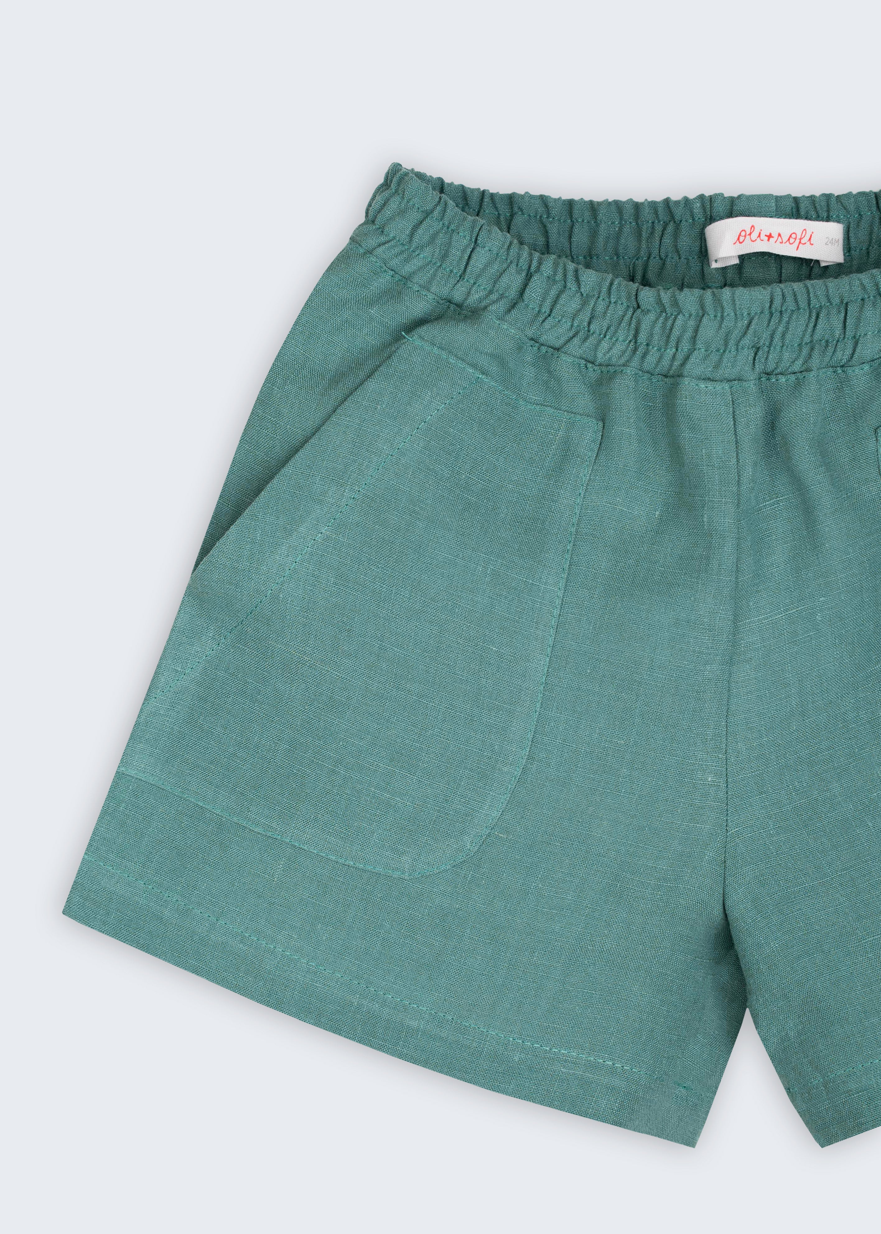 Detalhe do shorts infantil em linho verde com bolso frontal e textura natural do tecido