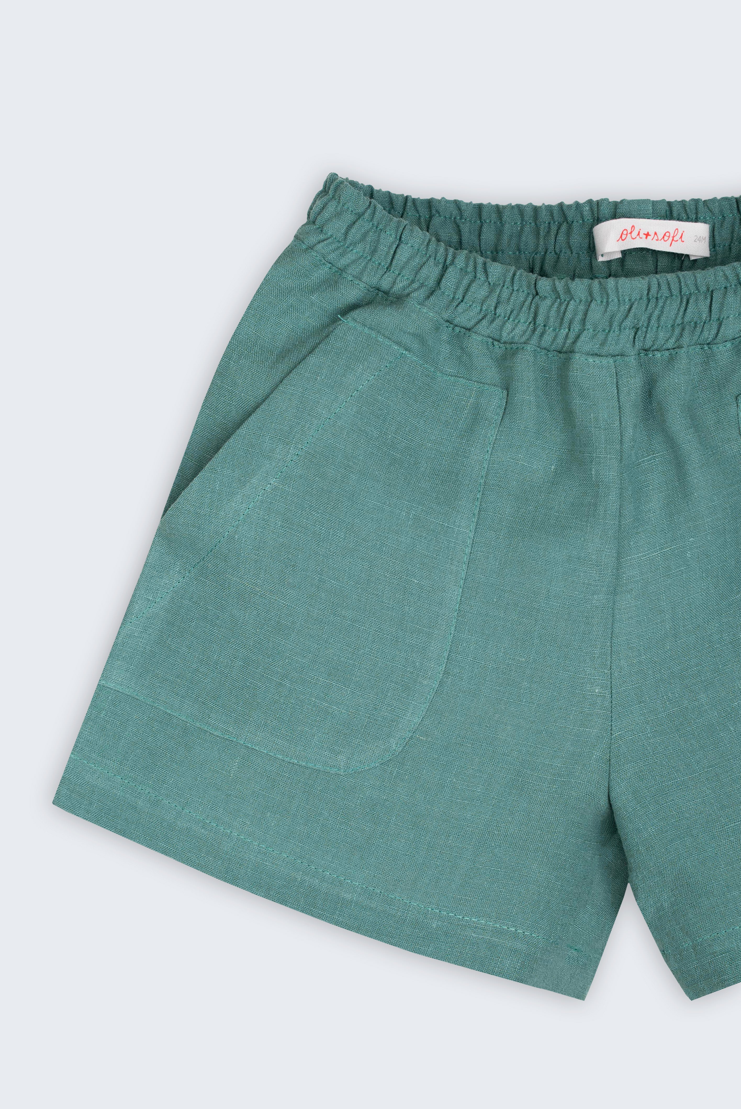 Detalhe do shorts infantil em linho verde com bolso frontal e textura natural do tecido