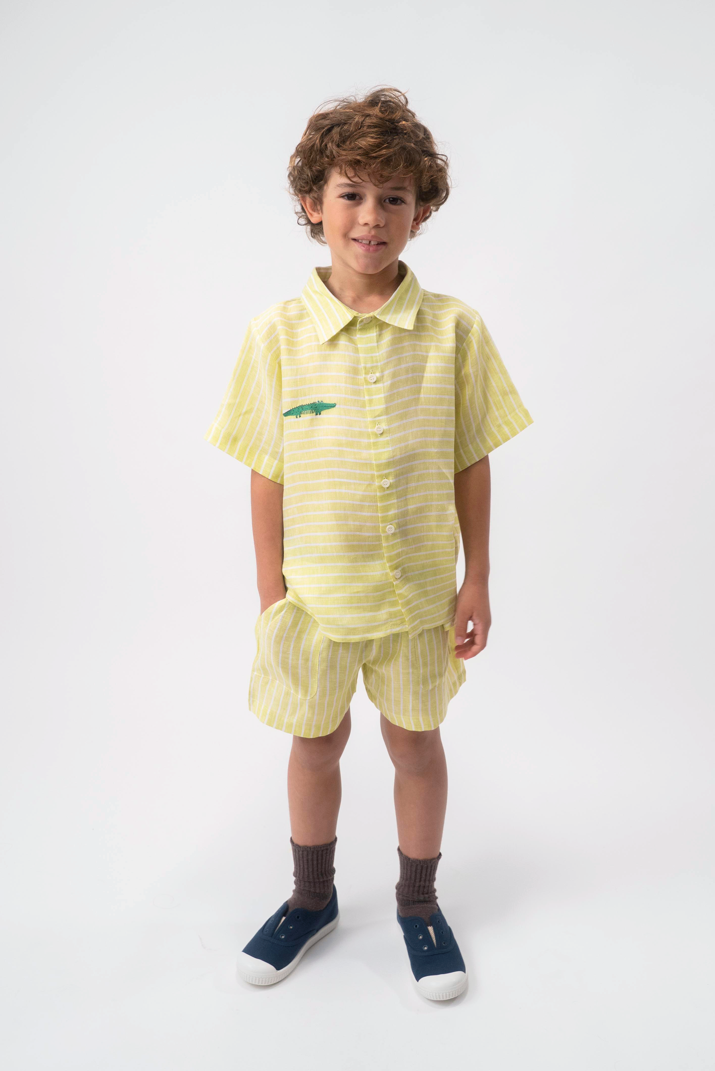 Menino vestindo Shorts Chico infantil em linho verde com listras brancas, combinado com camisa no mesmo tecido.