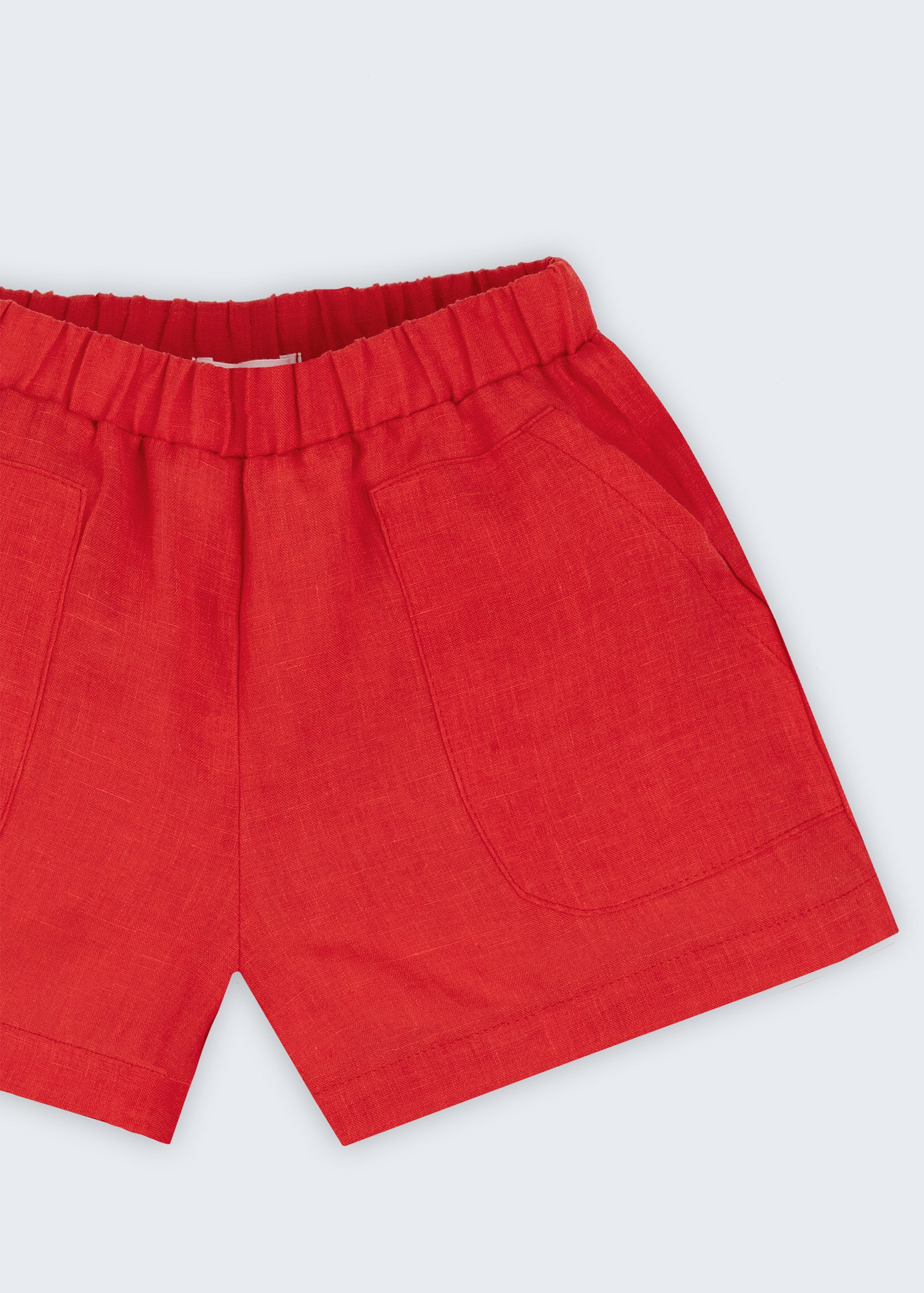 Close de shorts infantil em linho puro vermelho com bolsos frontais e cintura elástica.