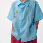 Detalhe do Shorts Chico infantil em linho vinho com bolsos frontais, usado por menino com camisa azul, modelo para menino e menina.