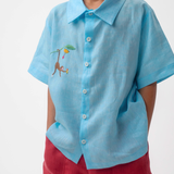 Detalhe do Shorts Chico infantil em linho vinho com bolsos frontais, usado por menino com camisa azul, modelo para menino e menina.