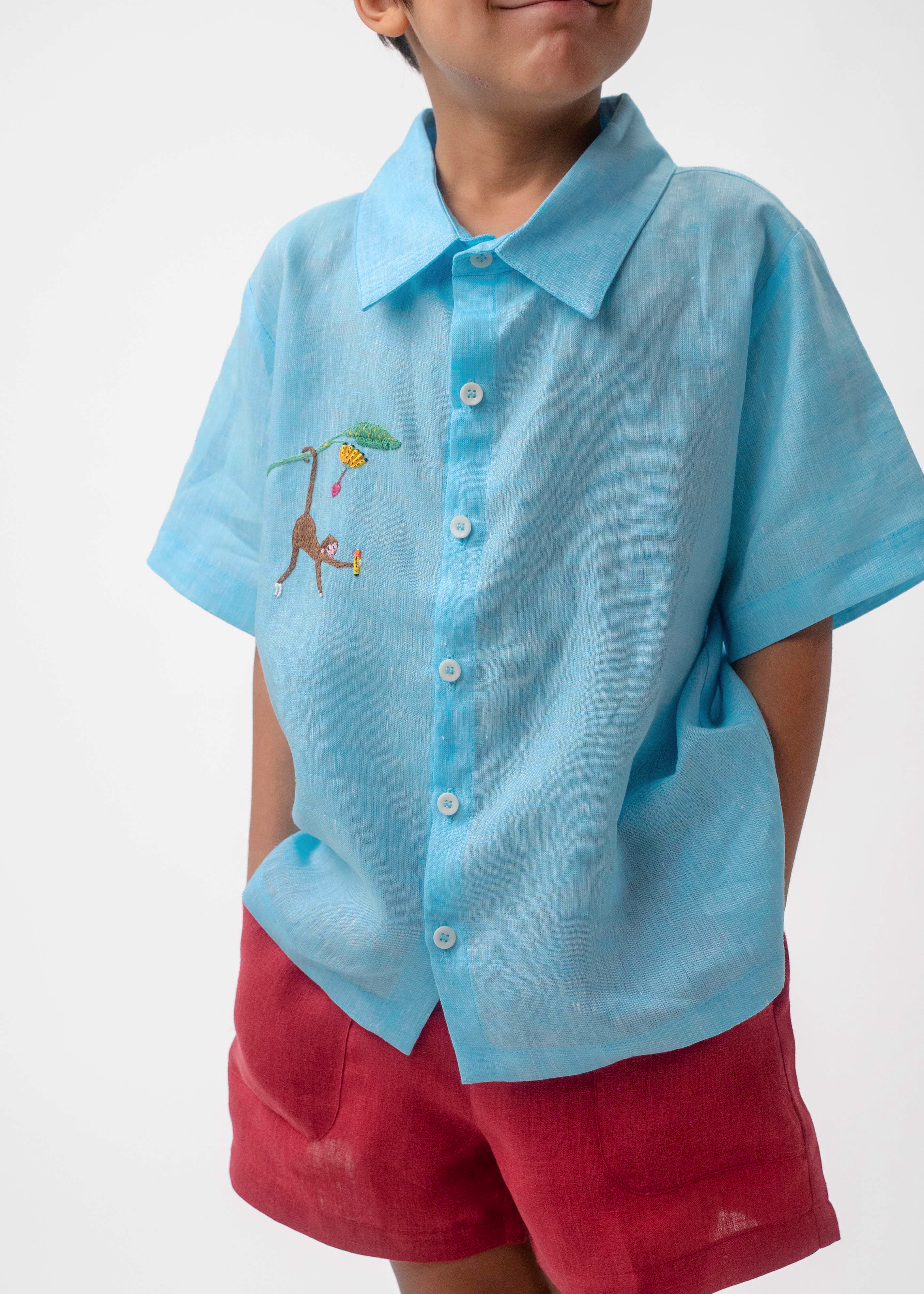 Detalhe do Shorts Chico infantil em linho vinho com bolsos frontais, usado por menino com camisa azul, modelo para menino e menina.