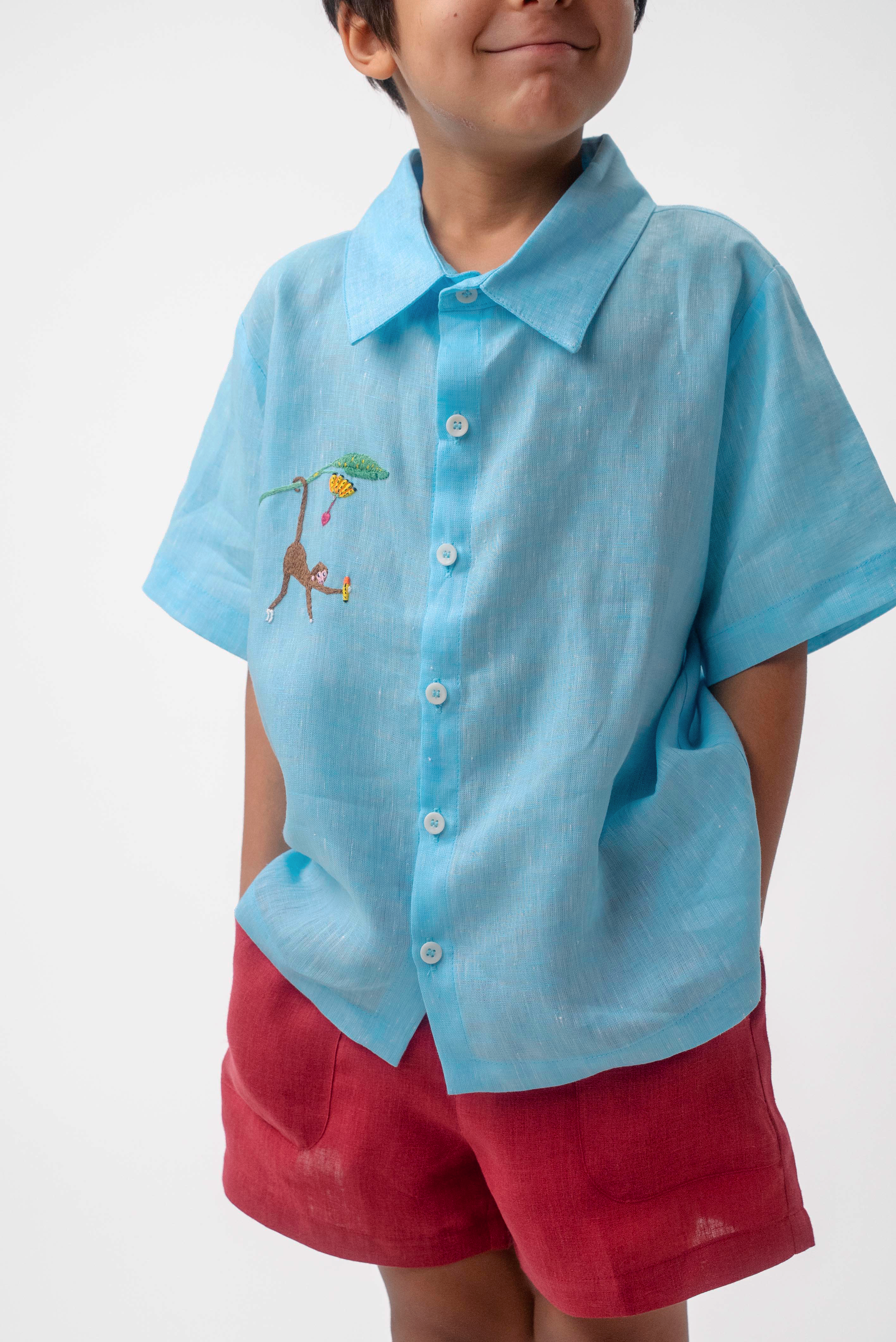 Detalhe do Shorts Chico infantil em linho vinho com bolsos frontais, usado por menino com camisa azul, modelo para menino e menina.