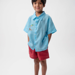 Menino vestindo Shorts Chico infantil em linho vinho com camisa azul, modelo de shorts para menino e menina em fundo branco.