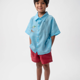 Menino vestindo Shorts Chico infantil em linho vinho com camisa azul, modelo de shorts para menino e menina em fundo branco.