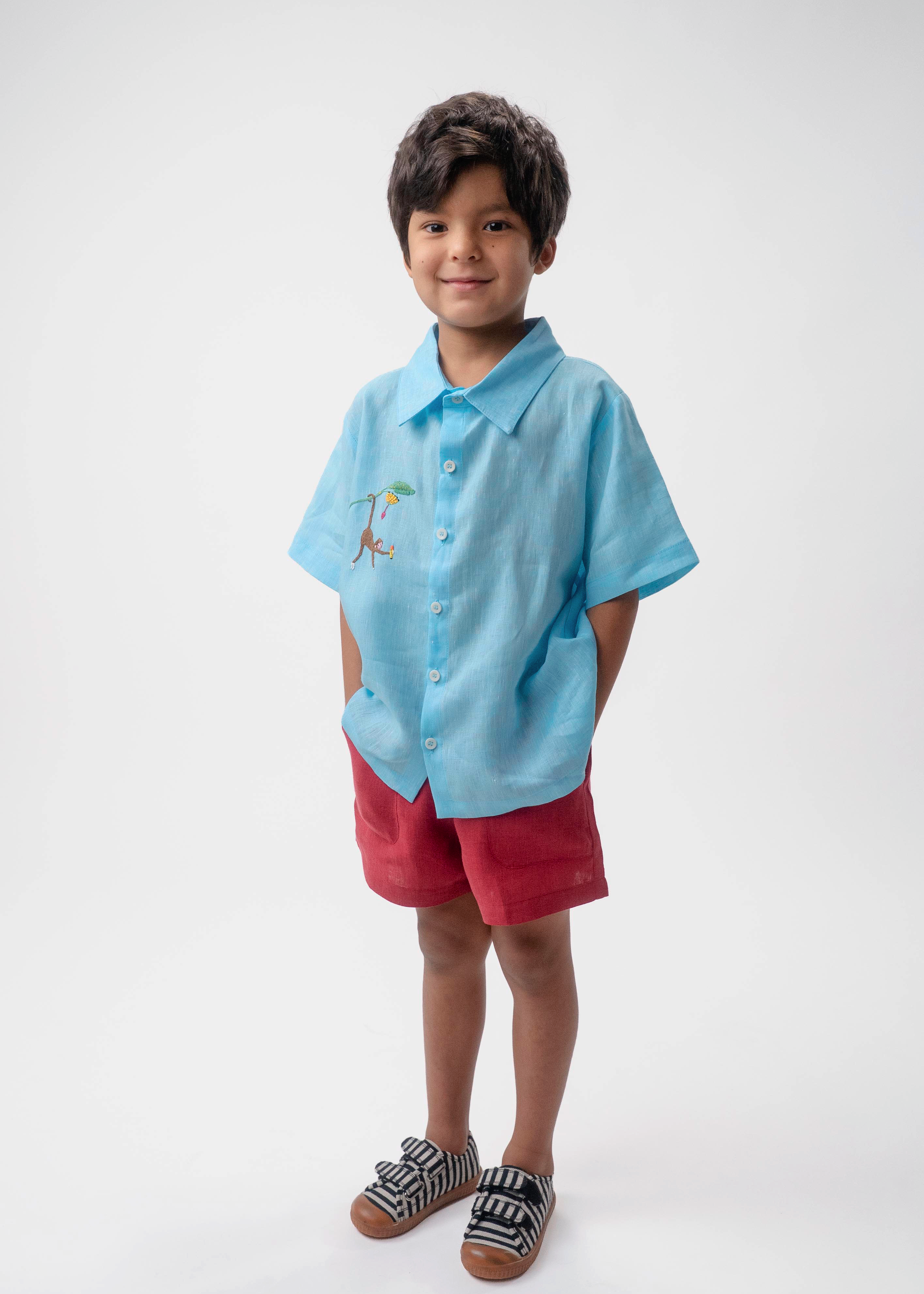 Menino vestindo Shorts Chico infantil em linho vinho com camisa azul, modelo de shorts para menino e menina em fundo branco.