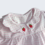 Detalhe da gola xadrez bordada de morangos vermelhos do vestido bebê em algodão listrado branco e rosa.