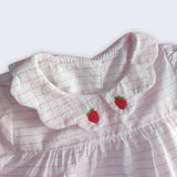 Detalhe da gola xadrez bordada de morangos vermelhos do vestido bebê em algodão listrado branco e rosa.