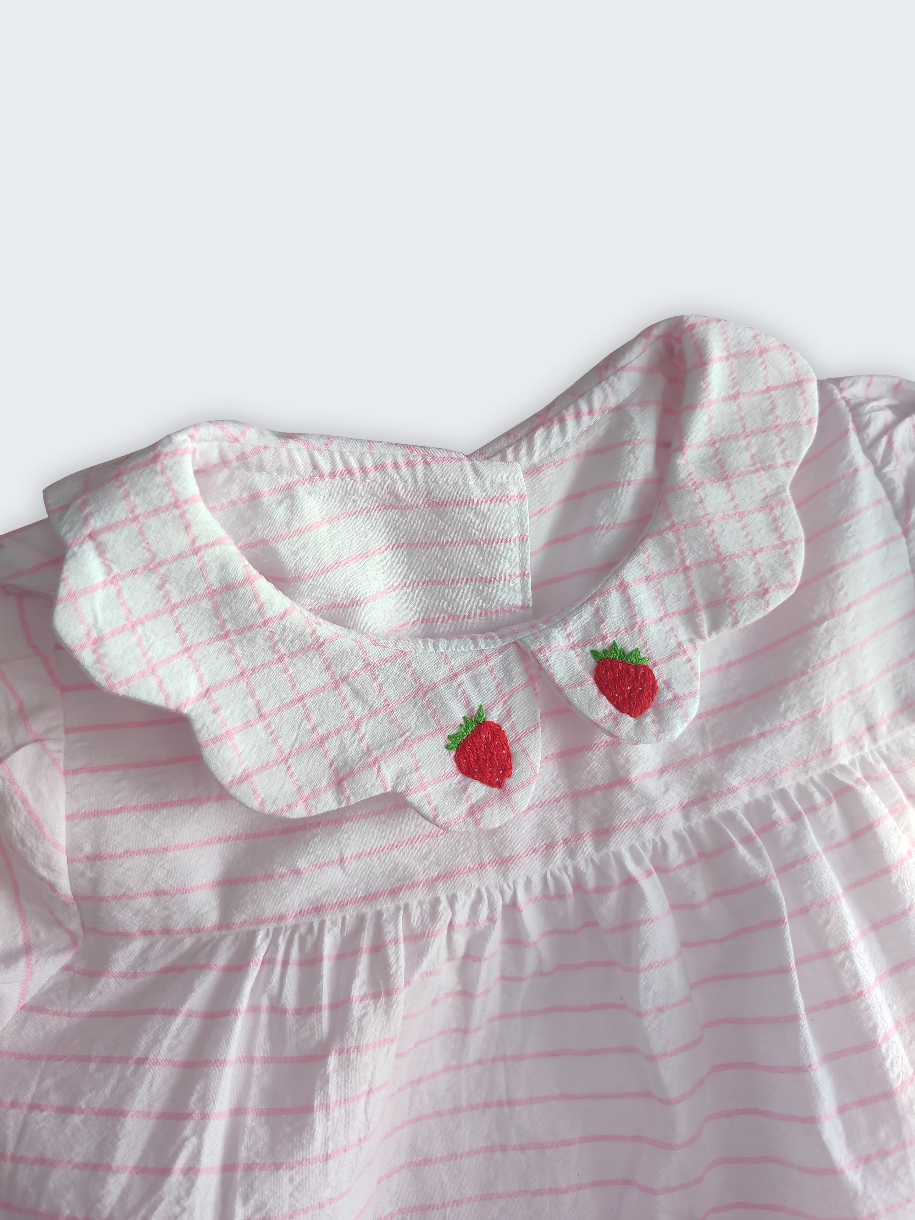 Detalhe da gola xadrez bordada de morangos vermelhos do vestido bebê em algodão listrado branco e rosa.