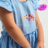 Detalhe menina usando vestido infantil em linho azul-celeste com bordado de flores e mangas e saia drapeadas