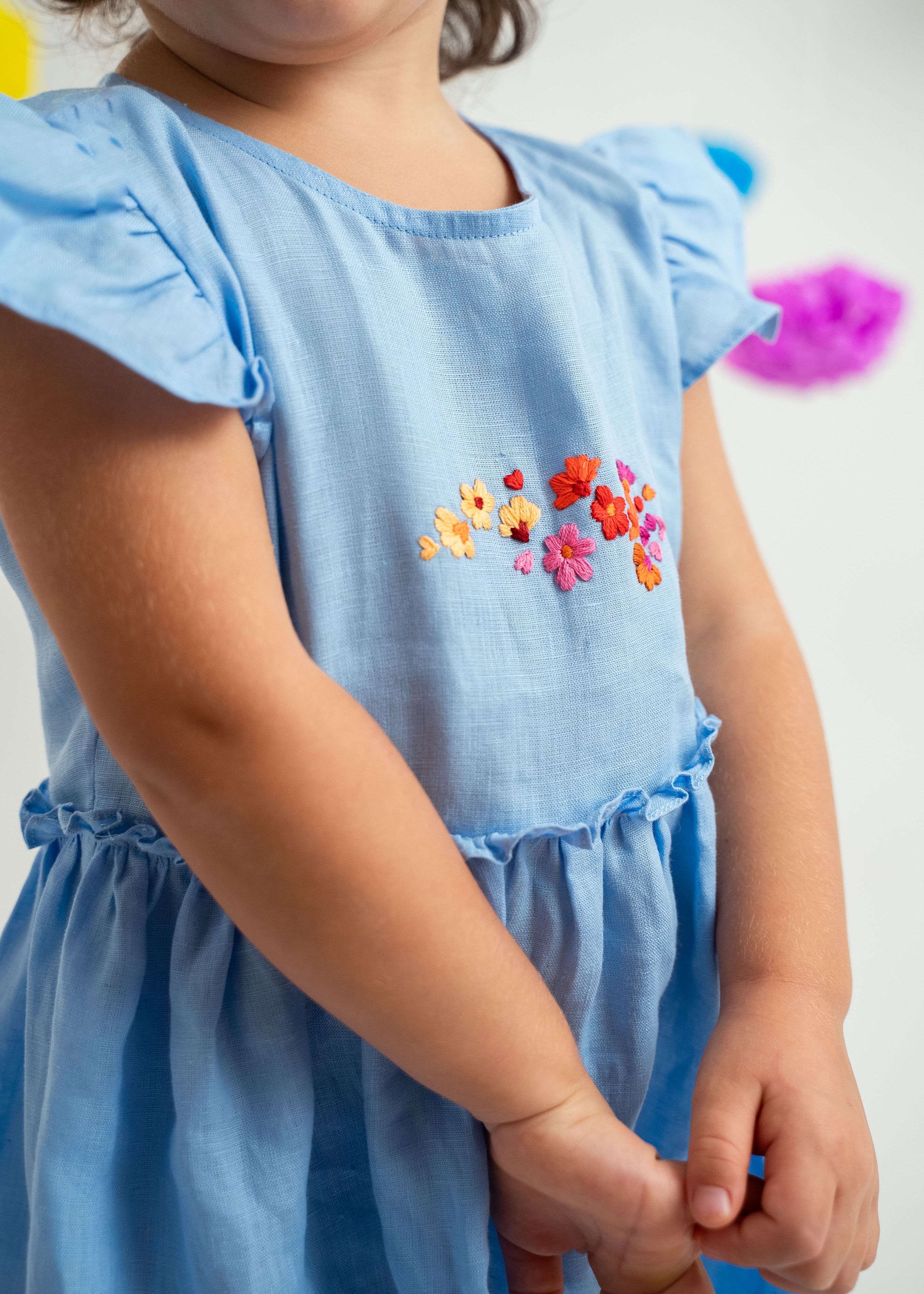 Detalhe menina usando vestido infantil em linho azul-celeste com bordado de flores e mangas e saia drapeadas