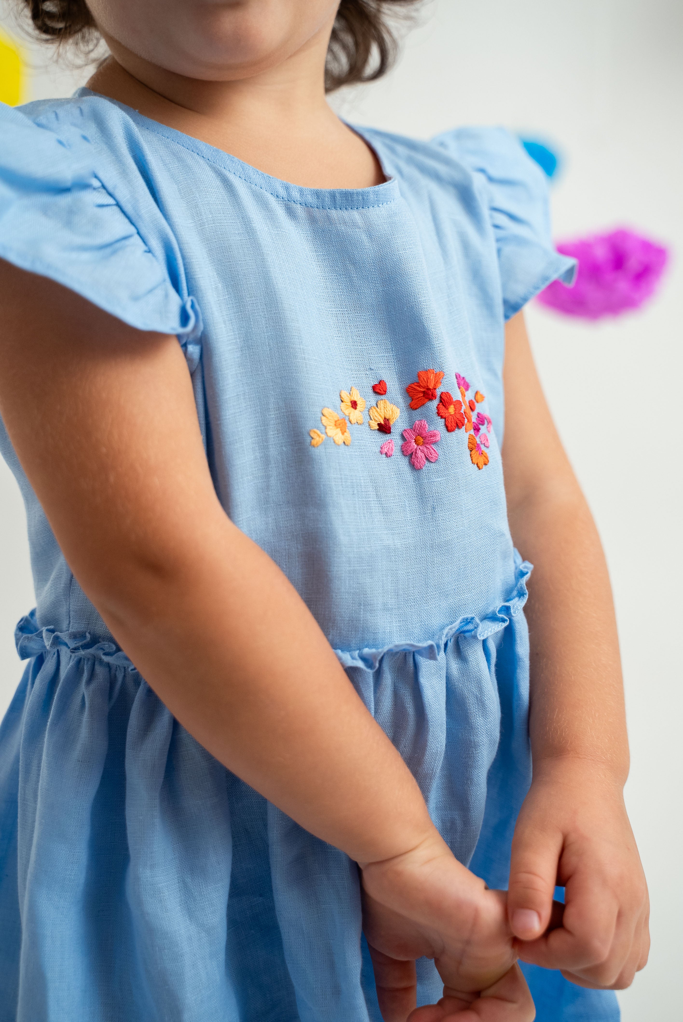 Detalhe menina usando vestido infantil em linho azul-celeste com bordado de flores e mangas e saia drapeadas