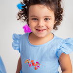 Menina usando vestido infantil em linho azul-celeste com bordado de flores e mangas drapeadas
