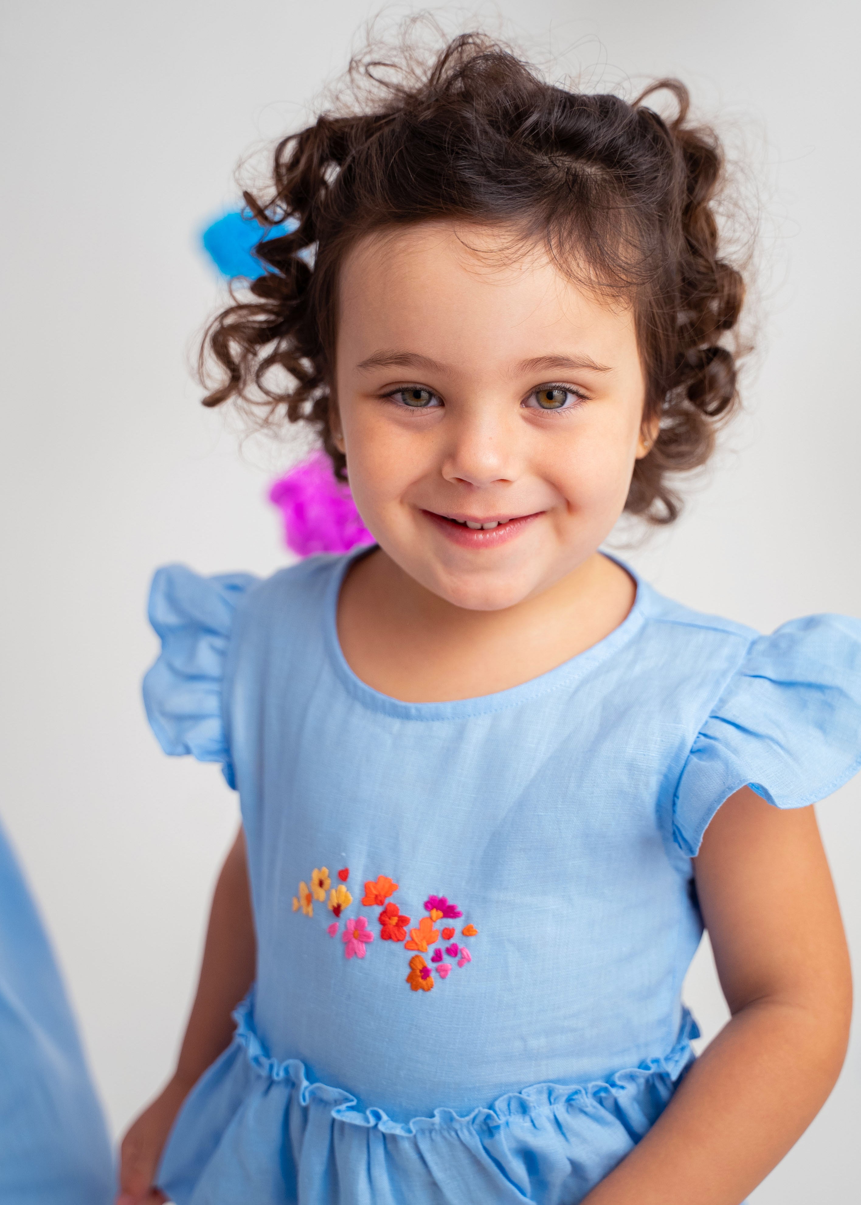 Menina usando vestido infantil em linho azul-celeste com bordado de flores e mangas drapeadas