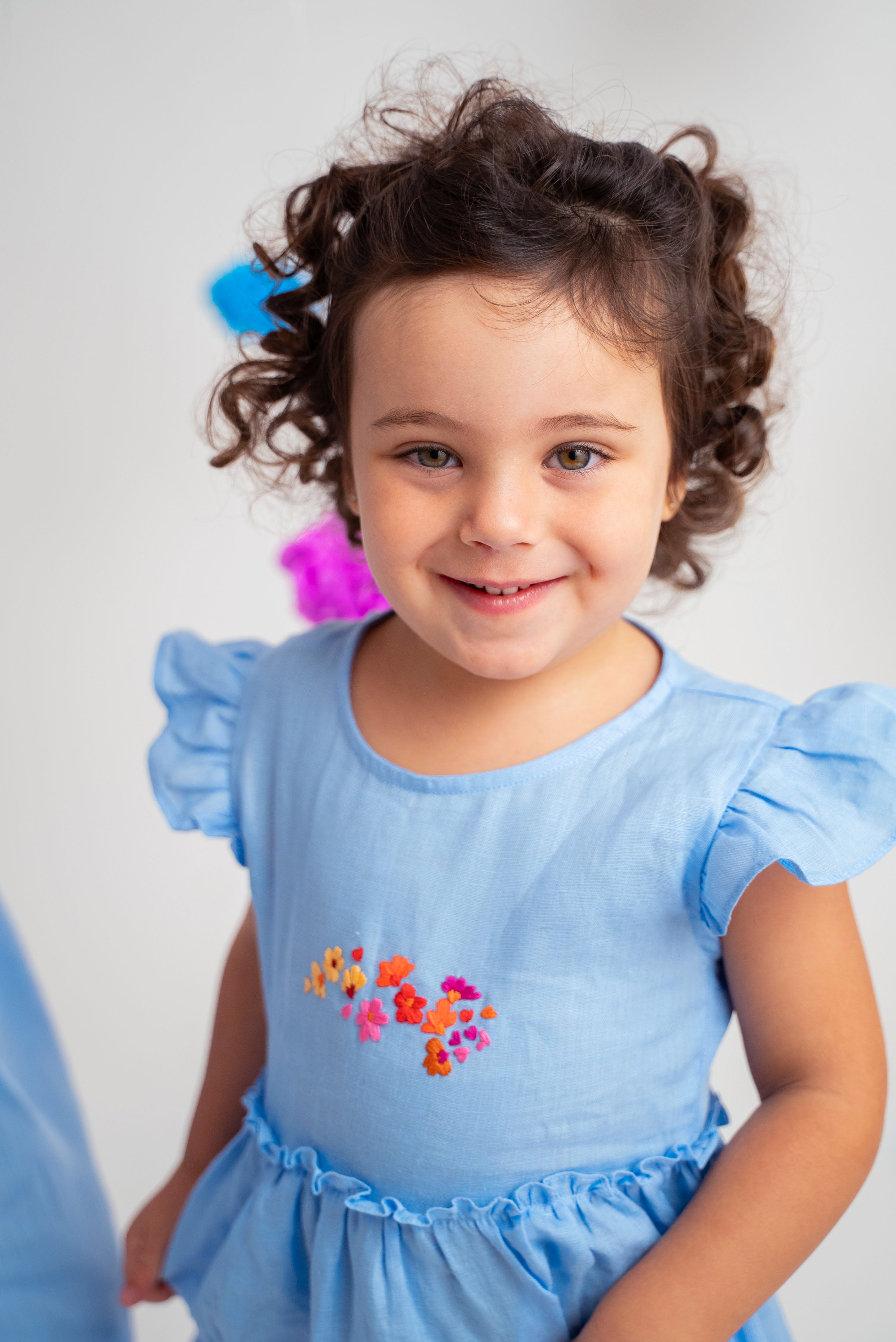 Menina usando vestido infantil em linho azul-celeste com bordado de flores e mangas drapeadas