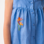 Detalhe do Vestido Clara em linho azul no corpo, mostrando trama texturizada, botões frontais e bordado de helicônia.