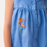 Detalhe do Vestido Clara em linho azul no corpo, mostrando trama texturizada, botões frontais e bordado de helicônia.