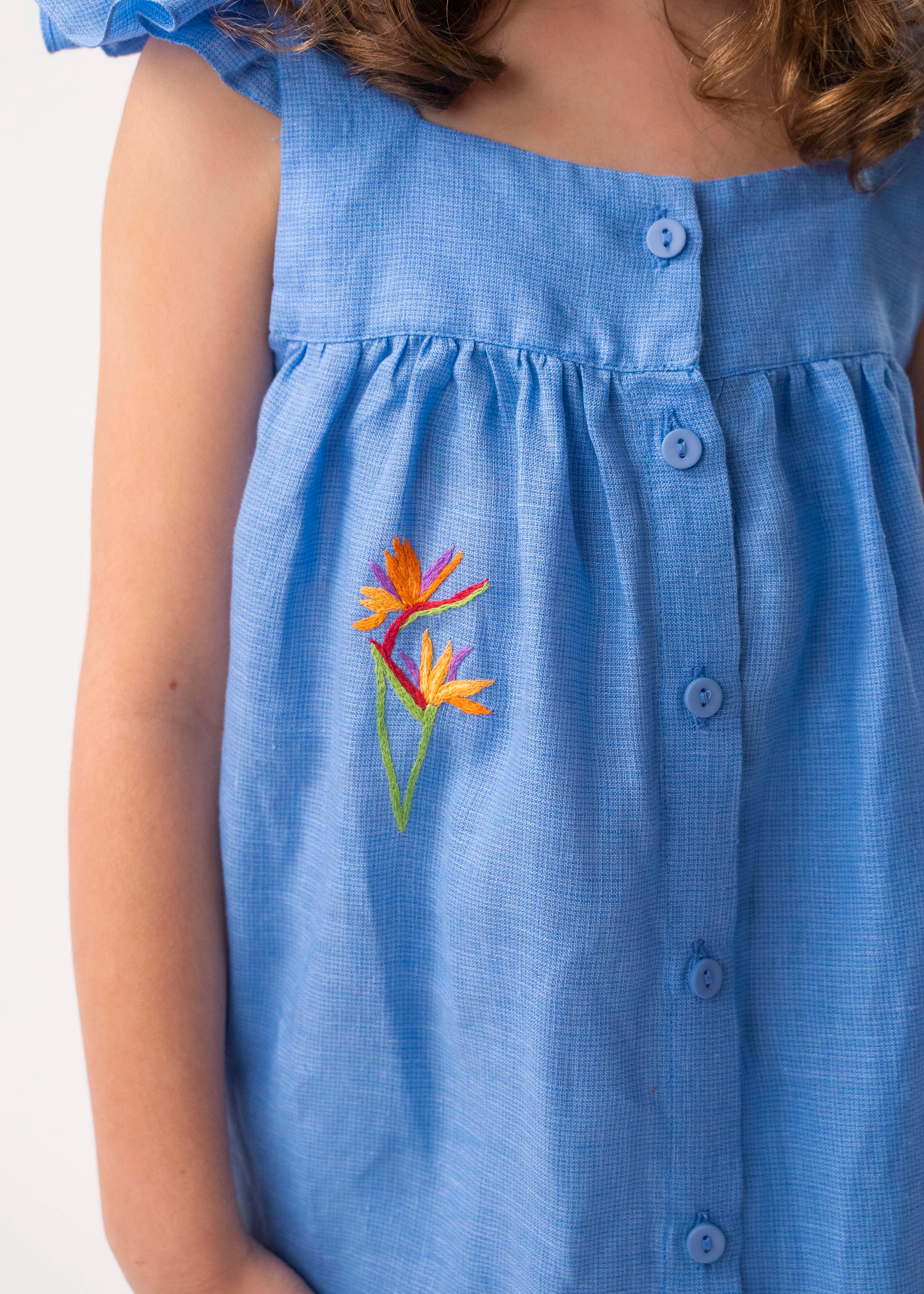 Detalhe do Vestido Clara em linho azul no corpo, mostrando trama texturizada, botões frontais e bordado de helicônia.