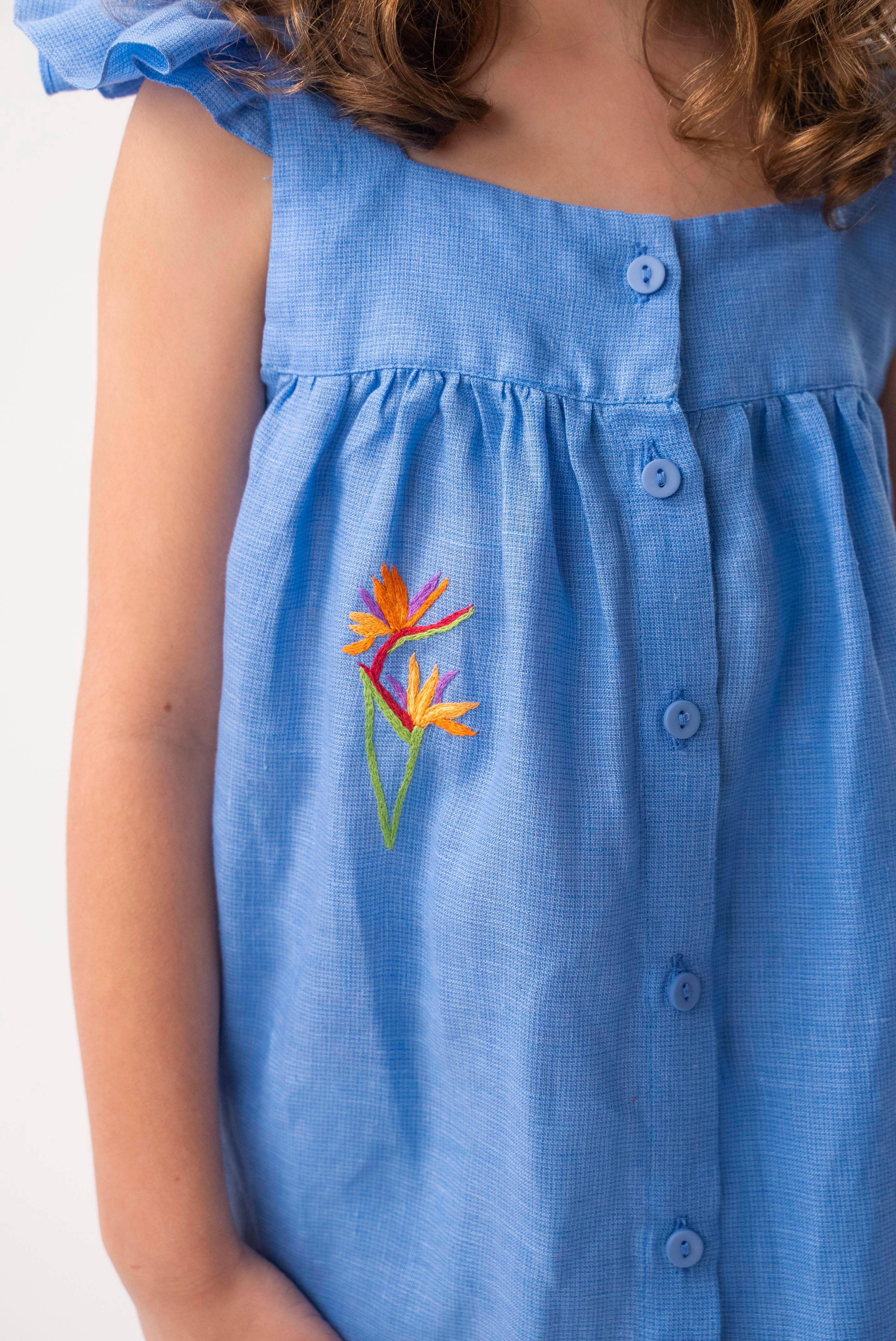 Detalhe do Vestido Clara em linho azul no corpo, mostrando trama texturizada, botões frontais e bordado de helicônia.