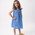 Menina vestindo Vestido Clara infantil em linho azul índigo com helicônia bordada à mão e mangas em babado.