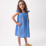 Menina vestindo Vestido Clara infantil em linho azul índigo com helicônia bordada à mão e mangas em babado.