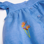 Detalhe do Vestido Clara em linho fio tinto azul índigo com helicônia bordada à mão, mangas em babado e botões frontais.