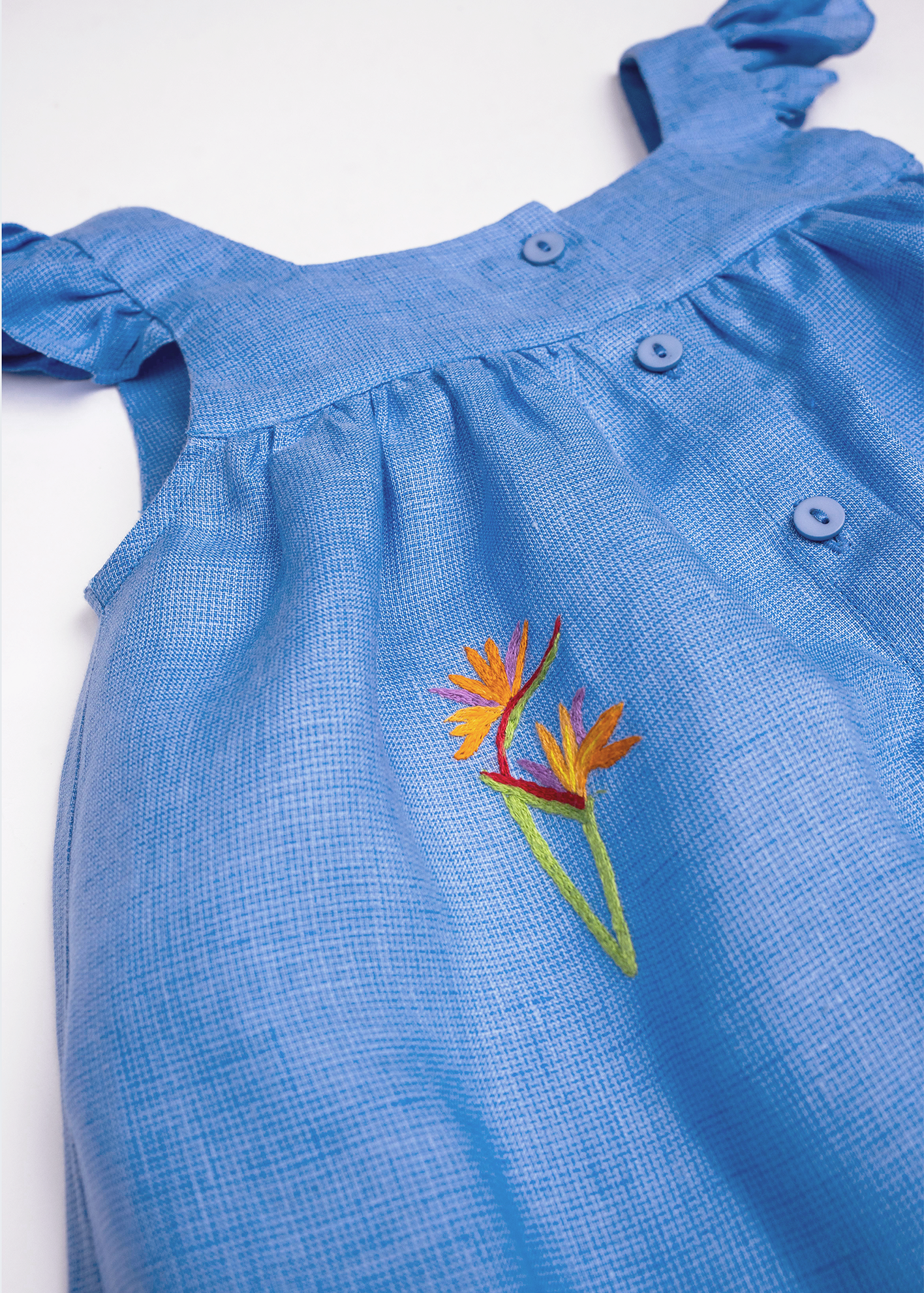 Detalhe do Vestido Clara em linho fio tinto azul índigo com helicônia bordada à mão, mangas em babado e botões frontais.