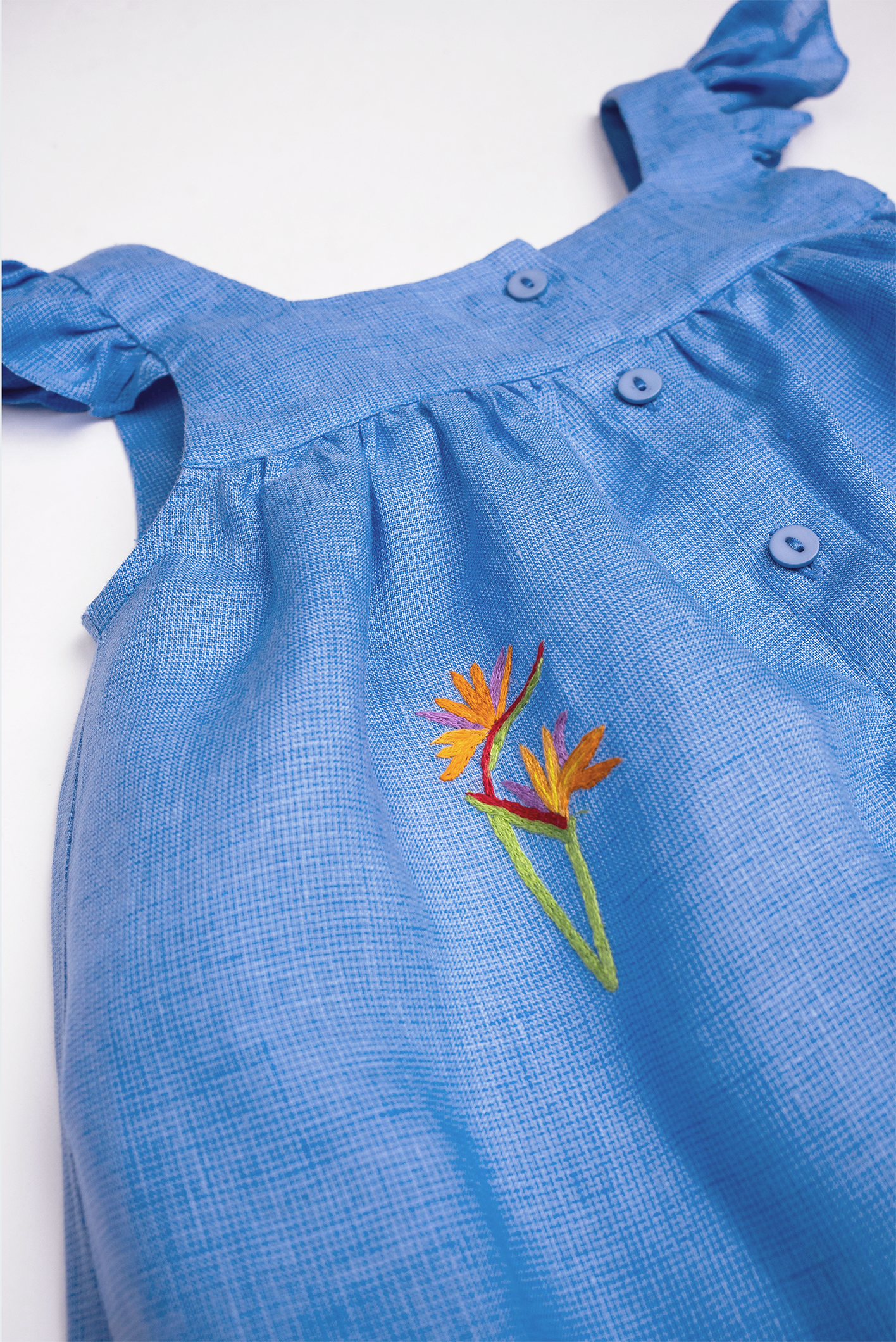 Detalhe do Vestido Clara em linho fio tinto azul índigo com helicônia bordada à mão, mangas em babado e botões frontais.