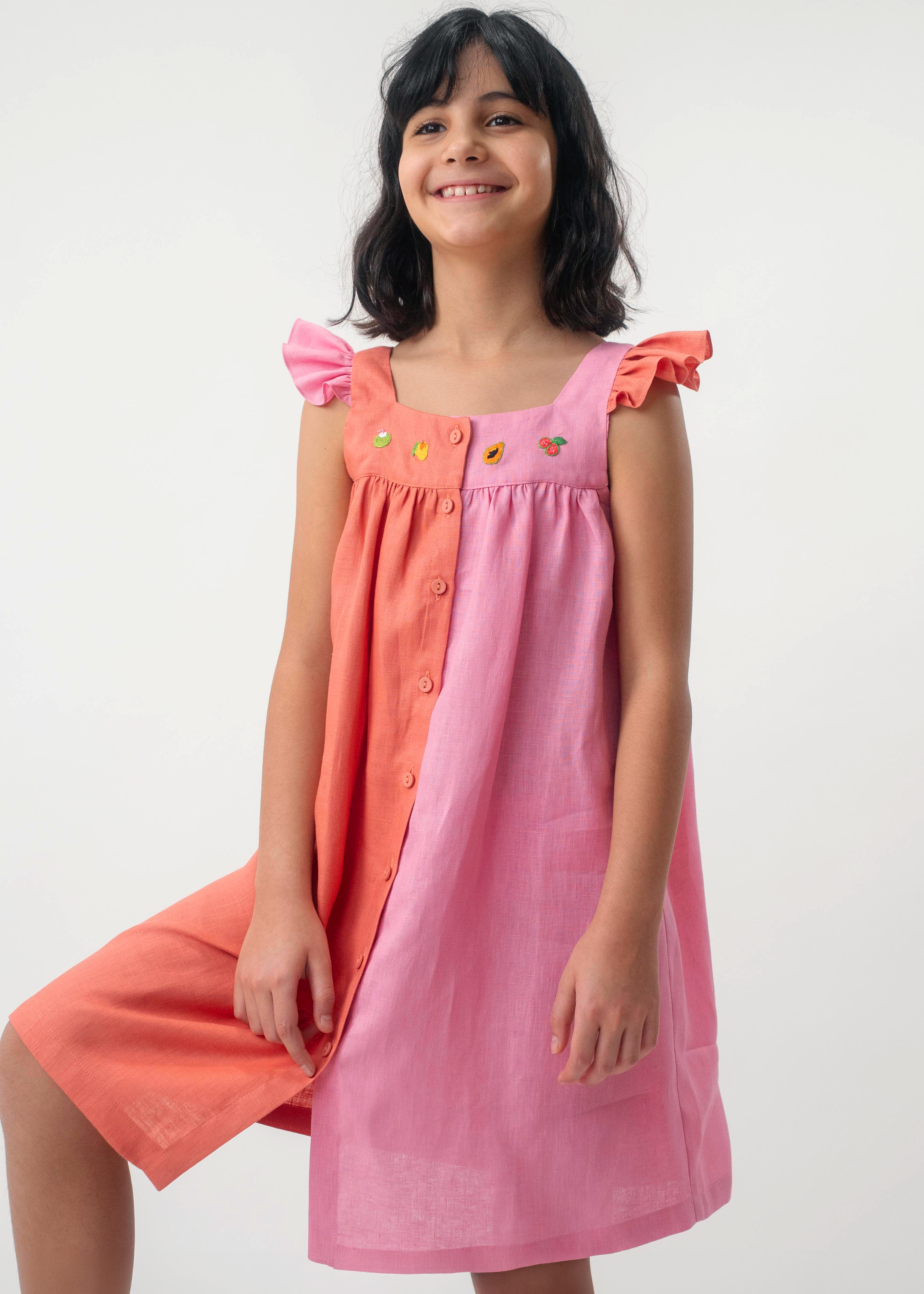 Menina vestindo Vestido Clara infantil em 100% linho rosa e coral, com frutas bordadas à mão e mangas em babado.