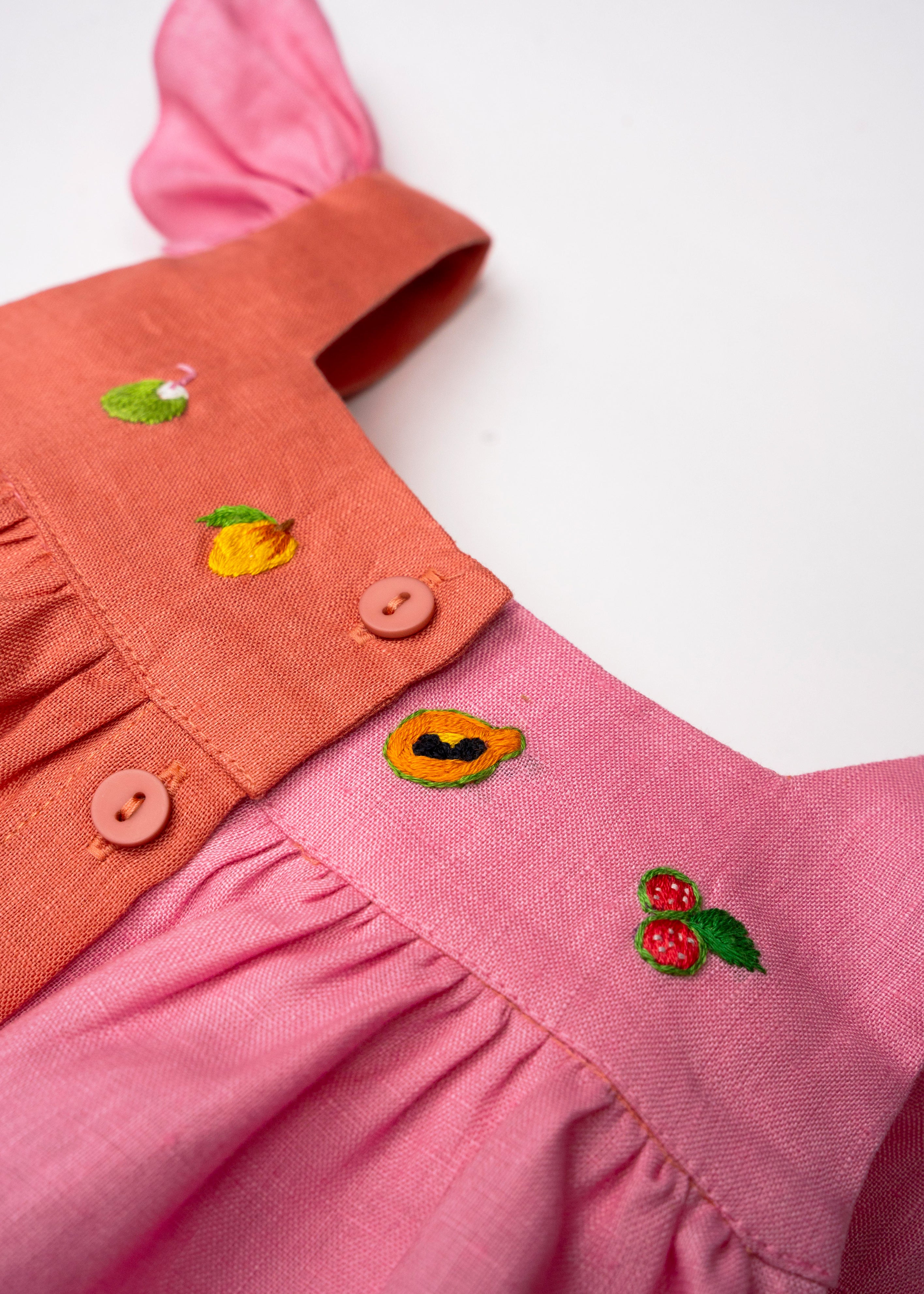 Detalhe das frutas bordadas à mão no Vestido Clara em linho bicolor rosa e coral, com botões frontais.