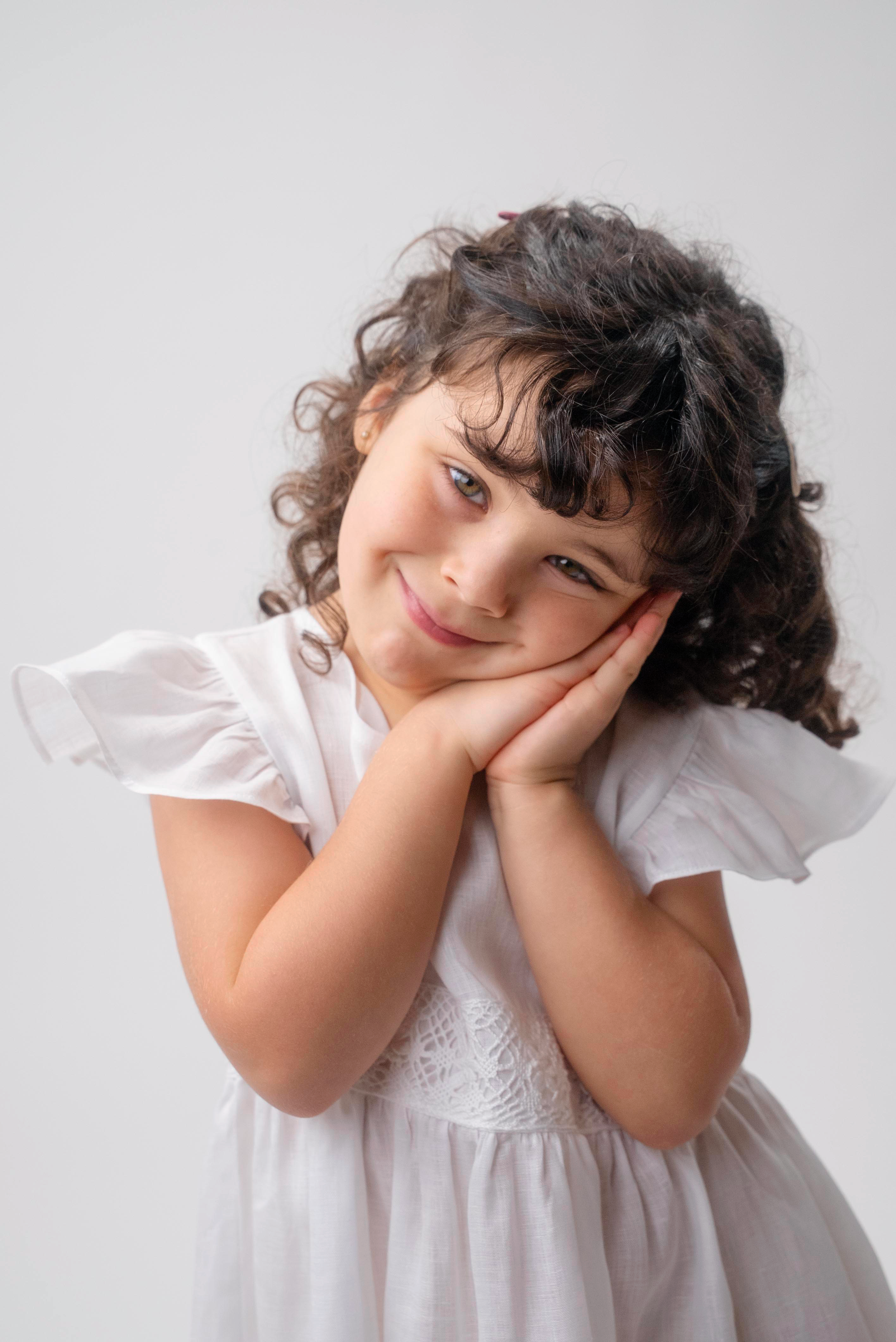 Detalhe da menina vestindo Vestido Clara em linho branco, com mangas em babado e faixa de renda de bilro.