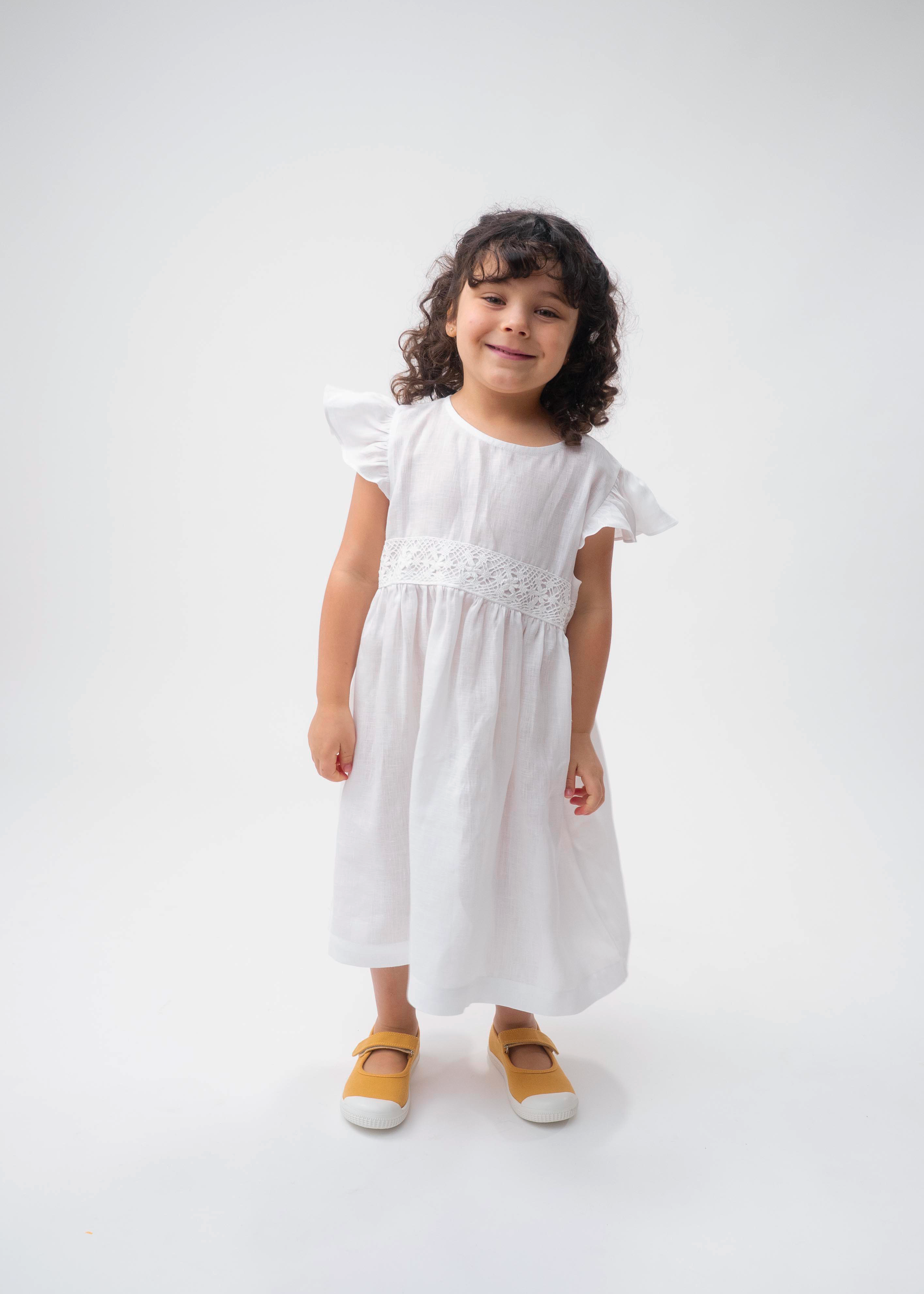 Menina vestindo Vestido Clara infantil em 100% linho branco com renda de bilro na cintura e mangas em babado.