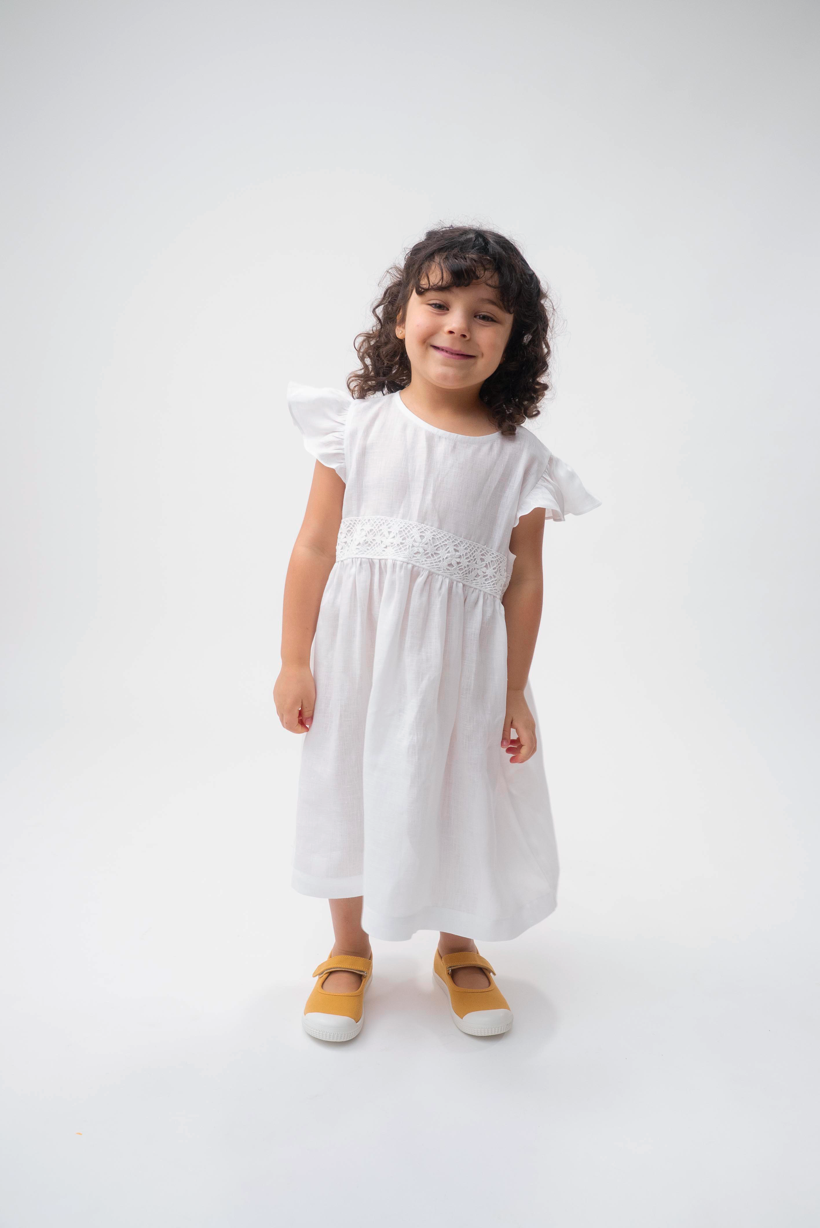 Menina vestindo Vestido Clara infantil em 100% linho branco com renda de bilro na cintura e mangas em babado.