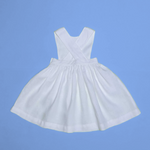 Vista de costas do vestido infantil de linho branco com alças cruzadas e saia ampla, em superfície azul.