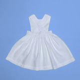 Vista de costas do vestido infantil de linho branco com alças cruzadas e saia ampla, em superfície azul.
